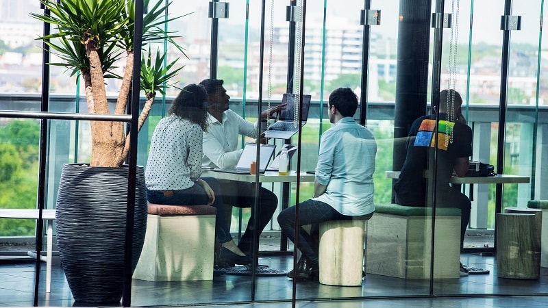 Cuatro personas colaborando en una oficina moderna con ventanas grandes y vistas de ciudad